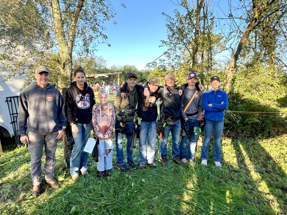 A group of archers and coaches standing together outdoors on a sunny day