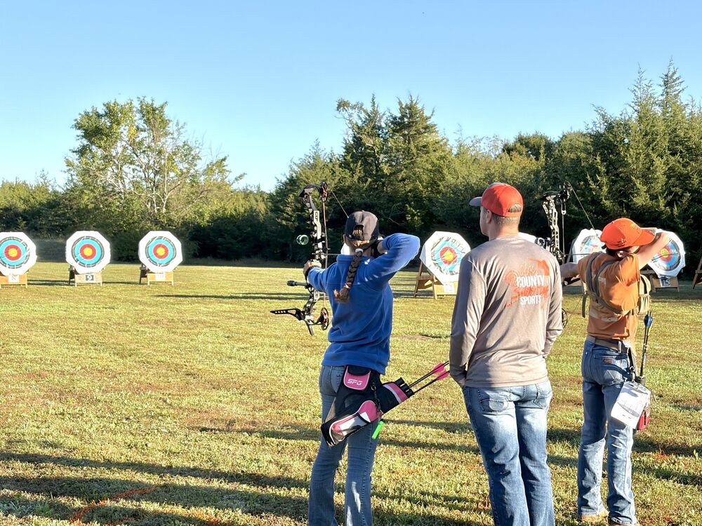 Archers shooting at target faces on the Clay County range as a coach looks on