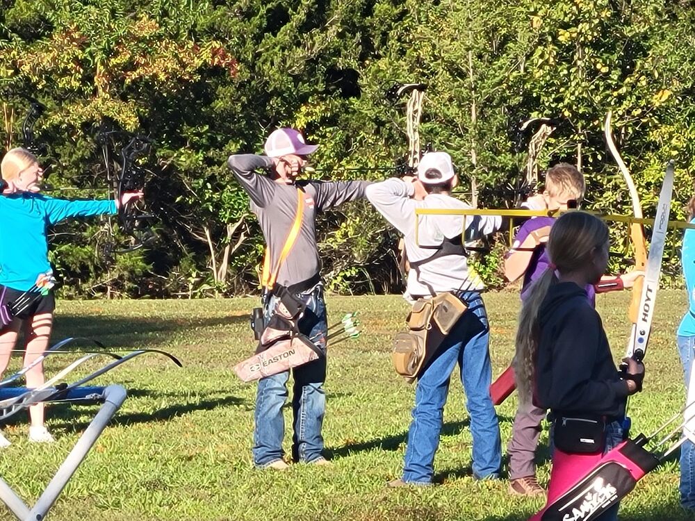 Young archers drawing their bows side by side on a grassy range