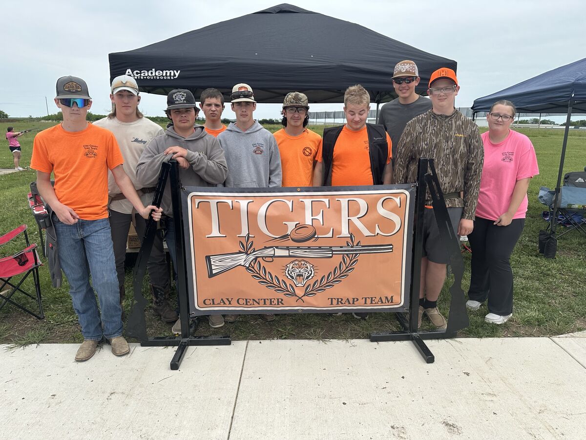 The Clay Center trap team in orange shirts posing behind a Tigers Clay Center Trap Team banner