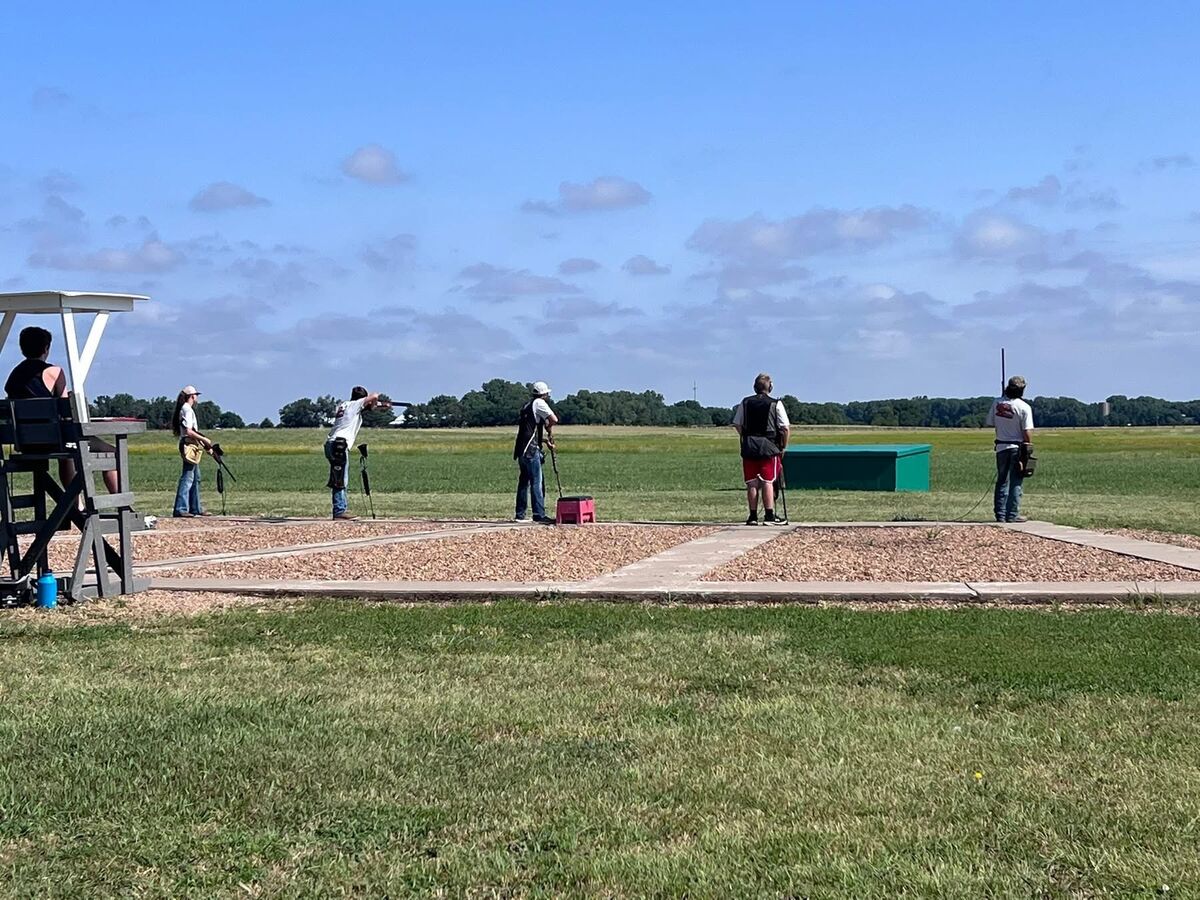 Trap shooters on the stations of a trap field under a wide blue sky