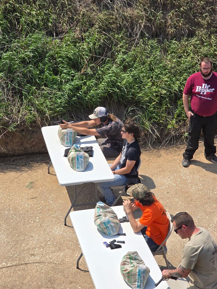 Shooters seated at folding tables with sandbag rests on an outdoor smallbore line, seen from above