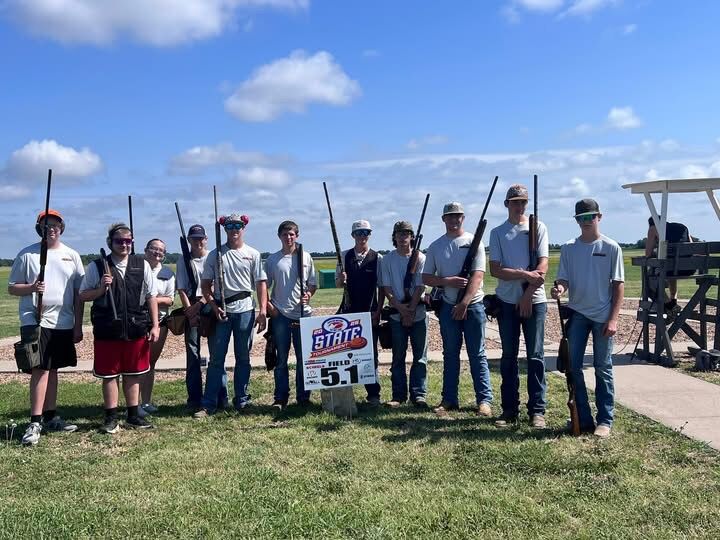 A line of trap shooters holding shotguns at the state tournament under a blue sky