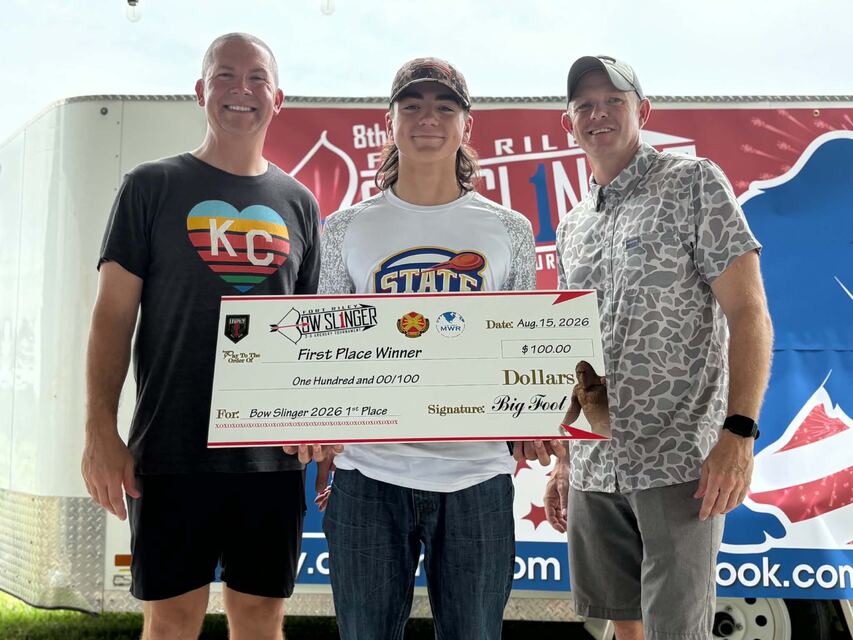 A club archer holding a first-place check from the Fort Riley Bow Slinger 2026 archery tournament with two adults