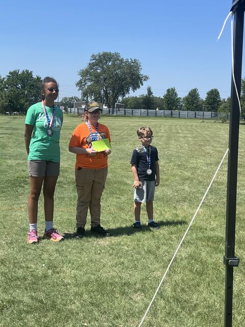 Three young shooters wearing medals and holding envelopes